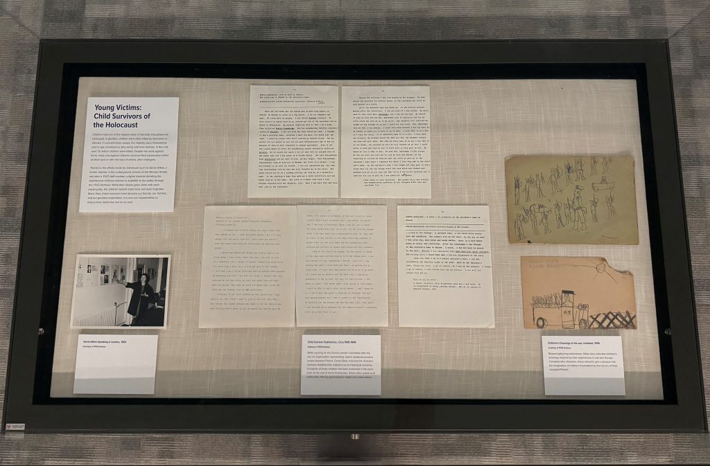 Overhead view of an exhibition case with a photo, drawings, and transcripts on display